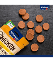 Vitakraft chicken coins dog treats, high-protein, grain-free with 95% chicken meat, on a slate surface.
