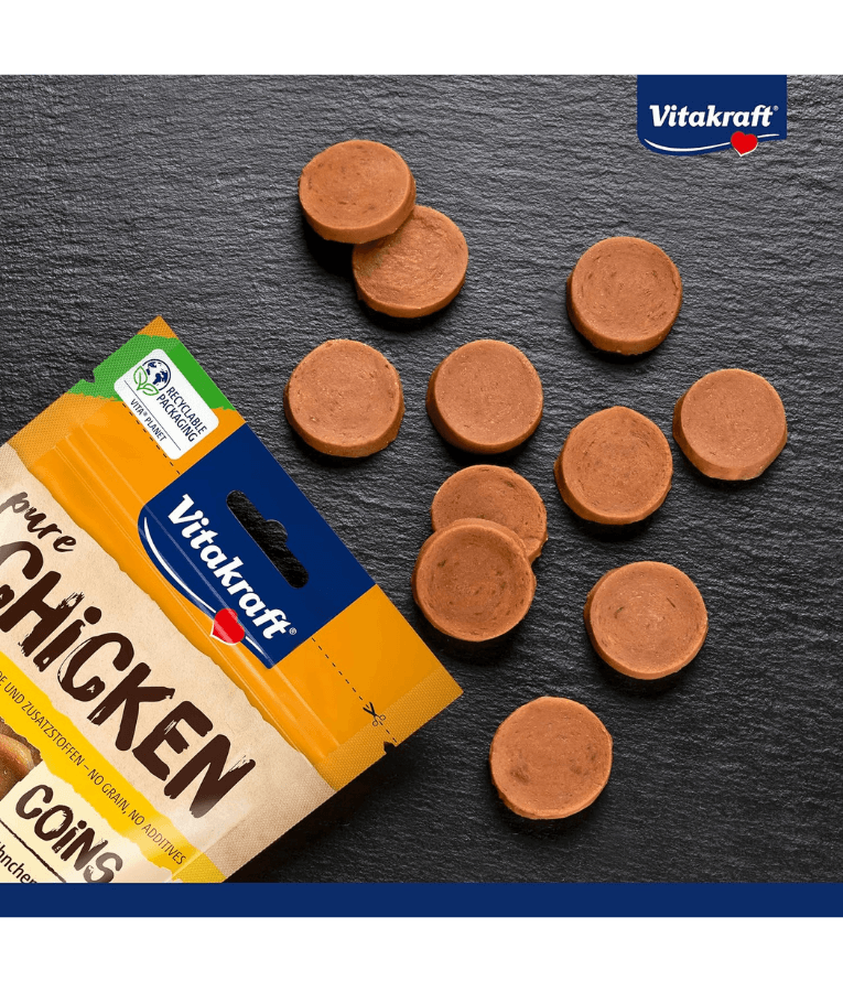 Vitakraft chicken coins dog treats, high-protein, grain-free with 95% chicken meat, on a slate surface.